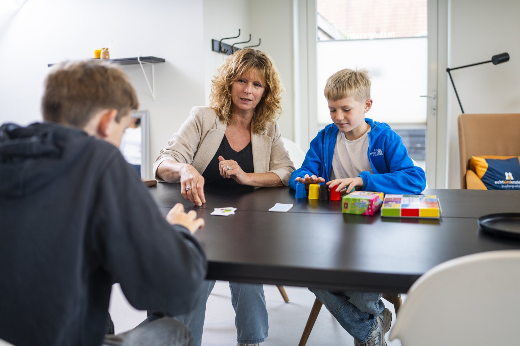 Behandelaar en jongen met spelmateriaal aan tafel